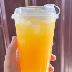 Foto es jeruk peras dalam gelas plastik bening bertutup, dipegang tangan
